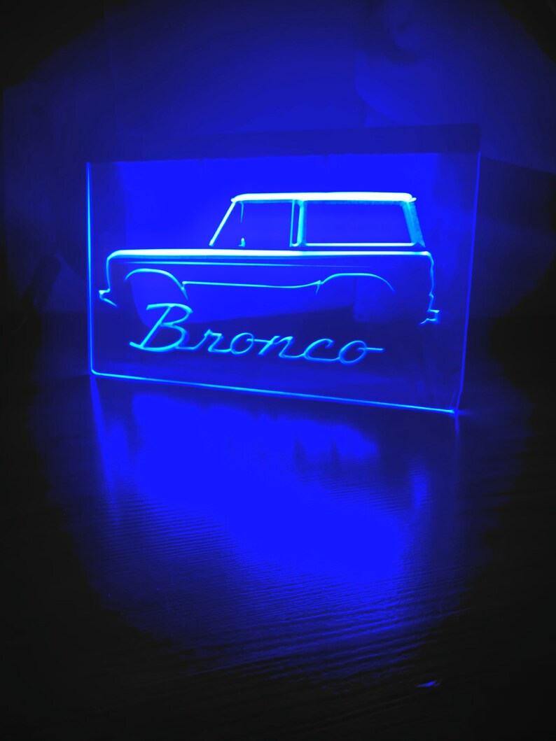 May include: A blue neon sign with the silhouette of a Ford Bronco and the word "Bronco" underneath.