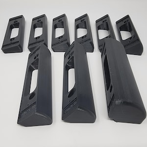 May include: A collection of nine black, rectangular mounting brackets. Each bracket has a large, rectangular opening and several smaller holes. The brackets are arranged on a white surface.