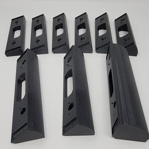 May include: A collection of black, rectangular door hardware components. The pieces have a long, narrow shape with a rectangular cutout and several small holes. The items are arranged on a white surface.