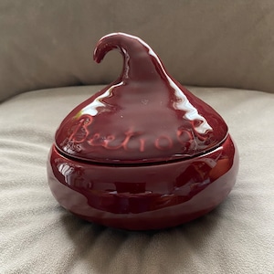 Puede incluir: Un recipiente de cerámica de color rojo oscuro con una tapa en forma de beso de Hershey. La tapa tiene la palabra "Beetroot" escrita en ella.
