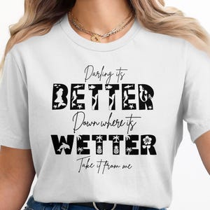 White t-shirt with black text "Darling it's BETTER Down Where it's WETTER" and beach graphics.
