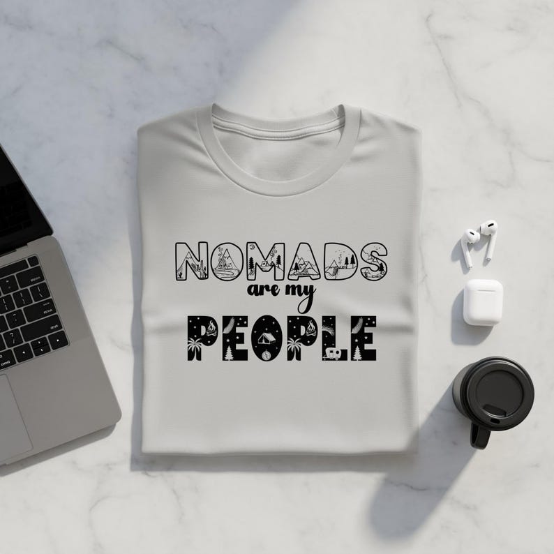 Gray t-shirt with "Nomads are my people" graphic, laptop, and coffee cup.