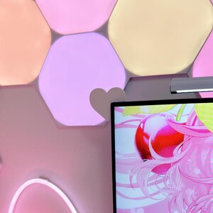 May include: A wall decorated with hexagon-shaped, color-changing LED lights in shades of pink, peach, and yellow. A heart-shaped accent is attached to the wall. A computer monitor displays a pink anime graphic.