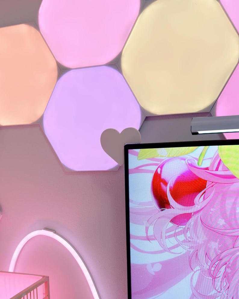 May include: A wall decorated with hexagon-shaped, color-changing LED lights in shades of pink, peach, and yellow. A heart-shaped accent is attached to the wall. A computer monitor displays a pink anime graphic.