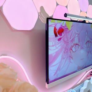 May include: A computer monitor displays a pink anime-style graphic. The monitor is mounted on a wall with pink hexagon-shaped lights. A pink neon light and a small keyboard are visible.