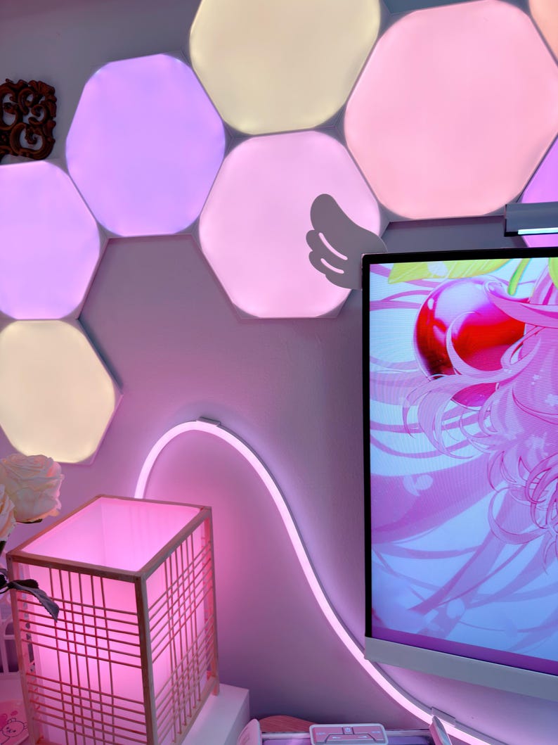 May include: A room with a pink and white aesthetic. Hexagon-shaped LED lights in various shades of pink and white are mounted on the wall. A pink neon light curves along the wall. A pink lamp with a wooden frame sits on a white surface.