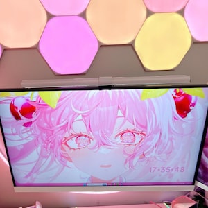 May include: A computer monitor displays a pink anime-style character with cherry accents and the time 17:35:48. The monitor is mounted on a wall with a light fixture and decorative wing accents. Hexagon-shaped lights in pink, yellow, and orange are above.