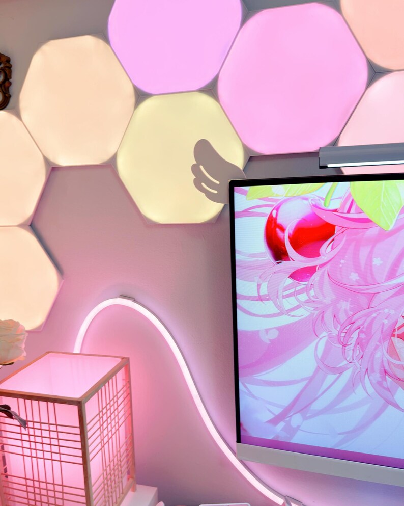 May include: A pink-themed room with a computer monitor displaying a pink anime graphic. A pink neon light curves along the wall. A wooden lantern and hexagon-shaped wall lights add to the decor. The room has a modern, colorful aesthetic.