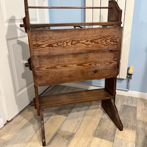 May include: A wooden folding table with a shelf and a top rail. The table is made of dark brown wood and has a rustic look.
