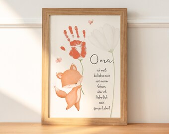 May include: A framed print with a handprint in orange, a fox illustration, and a white flower. The text reads "Oma, ich weiß du liebst mich seit meiner Geburt, aber ich liebe dich mein ganzes Leben!"