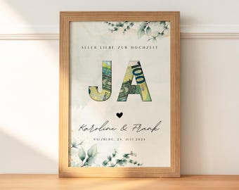 May include: A light brown wooden frame with a white background and green floral accents. The text "ALLES LIEBE ZUR HOCHZEIT" is at the top of the frame. The letters "JA" are made of euro bills. The text "Karoline & Frank" and "SALZBURG, 24. JULI 2024" are at the bottom of the frame.
