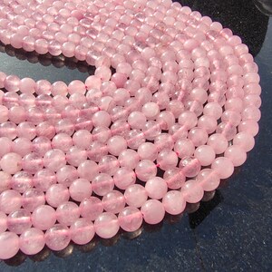 May include: A strand of pink rose quartz beads. The beads are round and smooth, and they have a translucent appearance. The beads are arranged in a circular pattern, and they are all the same size.