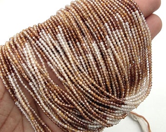 May include: A strand of brown and white faceted gemstone beads. The beads are small and round, and they are strung on a thin thread. The strand is long and is coiled up in a hand.