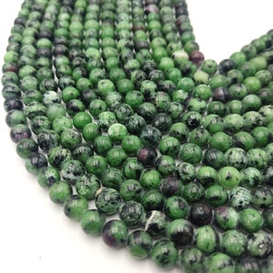 Könnte beinhalten: Eine Strähne grüner, schwarzer und rosafarbener Edelsteinperlen. Die Perlen sind rund und haben eine gesprenkelte Optik.