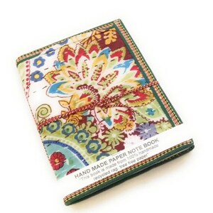 May include: A handmade paper notebook with a vibrant floral design. The cover displays a mix of red, yellow, blue, and green. The notebook is bound with a brown and red cord and has a green border. The label reads: "HAND MADE PAPER NOTE BOOK".