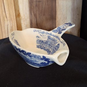 May include: A white and blue gravy boat with a handle. The boat has a blue floral pattern and the words "FAT", "GRAVY", and "LEAN" are printed on the rim. A blue and white landscape scene is also featured.