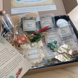 Op de afbeelding: Een doos met een prosperity spell jar kit. De kit bevat een glazen pot, gedroogd mos, groene aventurijn, bladgoud, laurier, wierookhars, kaneel en groene zegelwas. Een koperen lepel en een instructiekaart zijn ook inbegrepen.