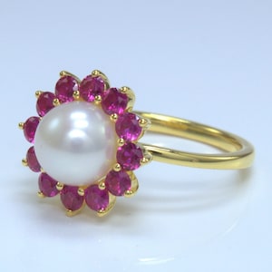 May include: A gold ring with a large white pearl surrounded by a halo of pink gemstones.