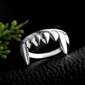 May include: Silver ring with a design of sharp teeth, resembling a vampire's fangs.