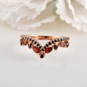 May include: A rose gold ring with a V-shaped design. The ring is adorned with small black gemstones and larger red gemstones.