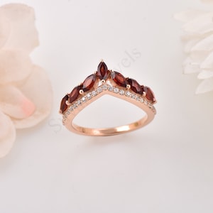 May include: A rose gold ring with a V-shaped band adorned with red marquise-shaped gemstones and smaller clear round gemstones.