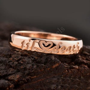Könnte beinhalten: Ein Roségold-Bandring mit der Inschrift "til death" und einem Herzsymbol.