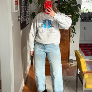 May include: A light gray sweatshirt with the text "NORTH CAROLINA" in a blue and white design. The sweatshirt is paired with light blue jeans and black platform boots. The outfit is casual and comfortable.