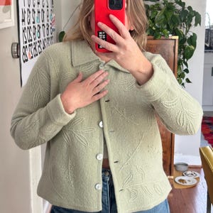 May include: A light green jacket with a leaf pattern. The jacket has a collared neckline, button closure, and long sleeves. The jacket is paired with blue jeans.