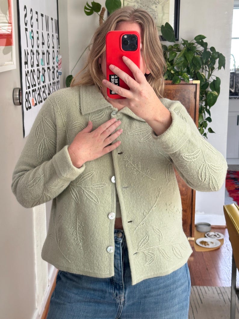 May include: A light green jacket with a leaf pattern. The jacket has a collared neckline, button closure, and long sleeves. The jacket is paired with blue jeans.