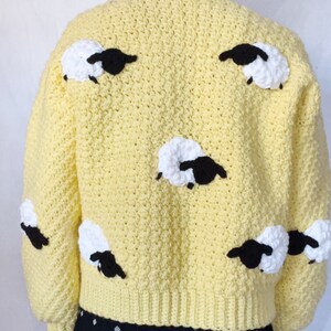 May include: A yellow crocheted sweater with black and white sheep appliques. The sweater has a crew neck and long sleeves.