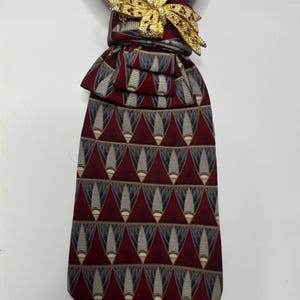 May include: A patterned necktie with a gold-colored bow tie pin. The tie features a repeating geometric design in burgundy, navy, and beige. The bow tie pin is a decorative accent.