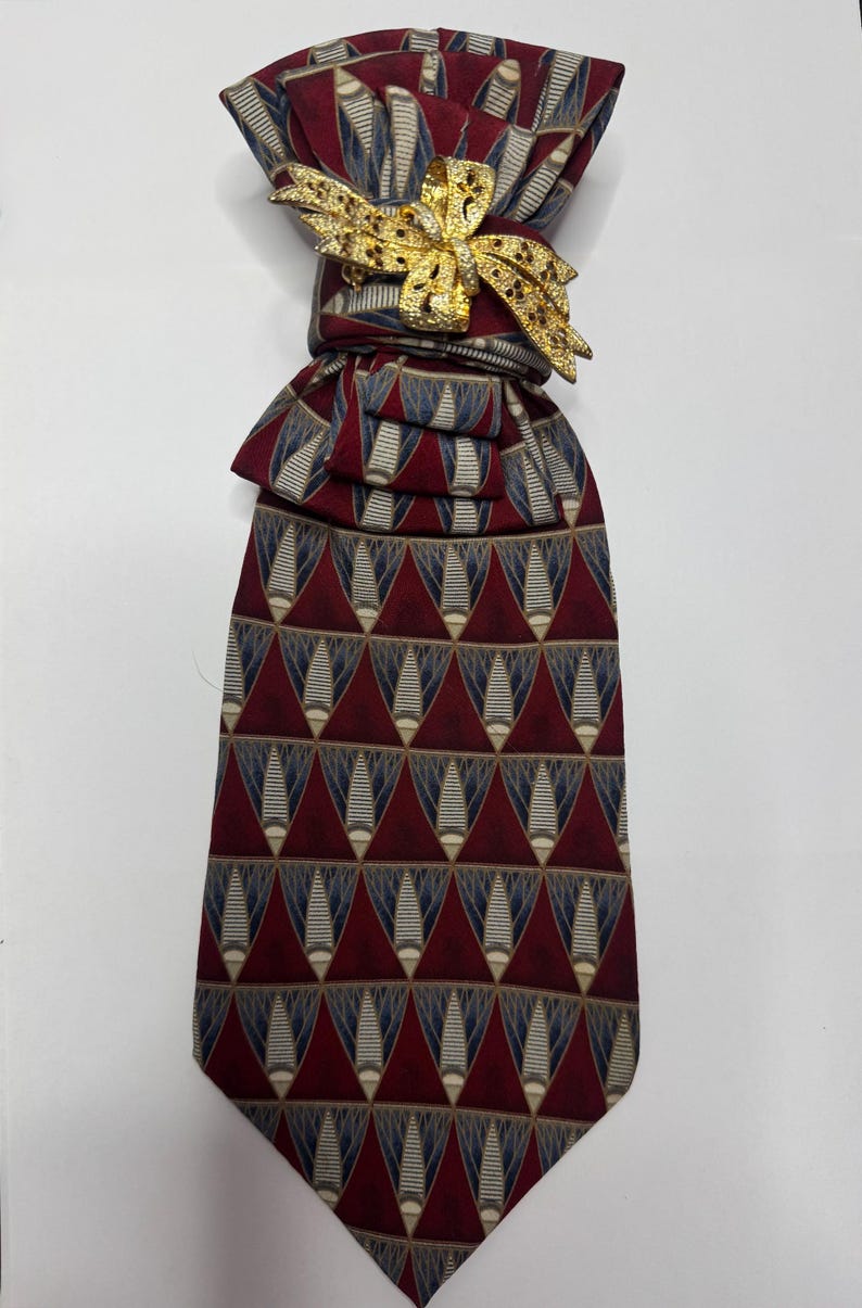 May include: A patterned necktie with a gold-colored bow tie pin. The tie features a repeating geometric design in burgundy, navy, and beige. The bow tie pin is a decorative accent.