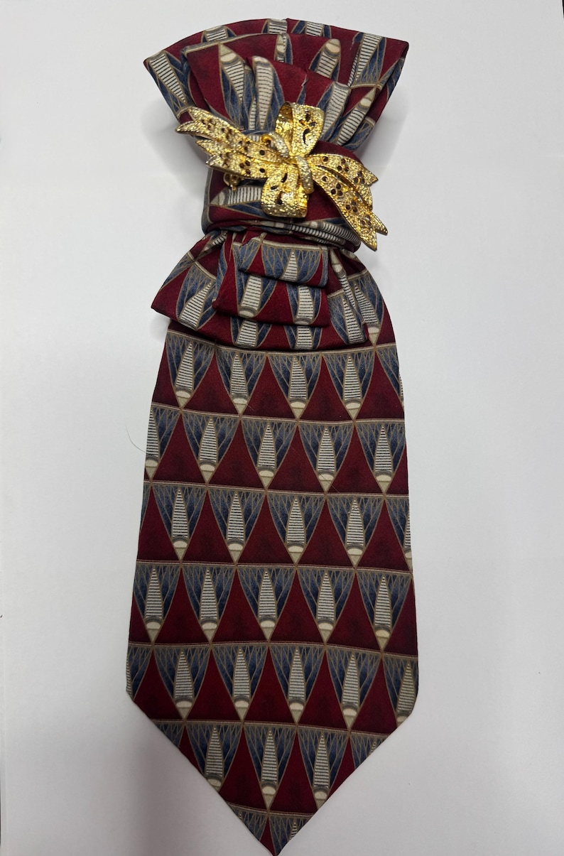 May include: A patterned necktie with a gold-colored bow tie pin. The tie features a repeating geometric design in burgundy, navy, and beige. The bow tie pin is a decorative accent.