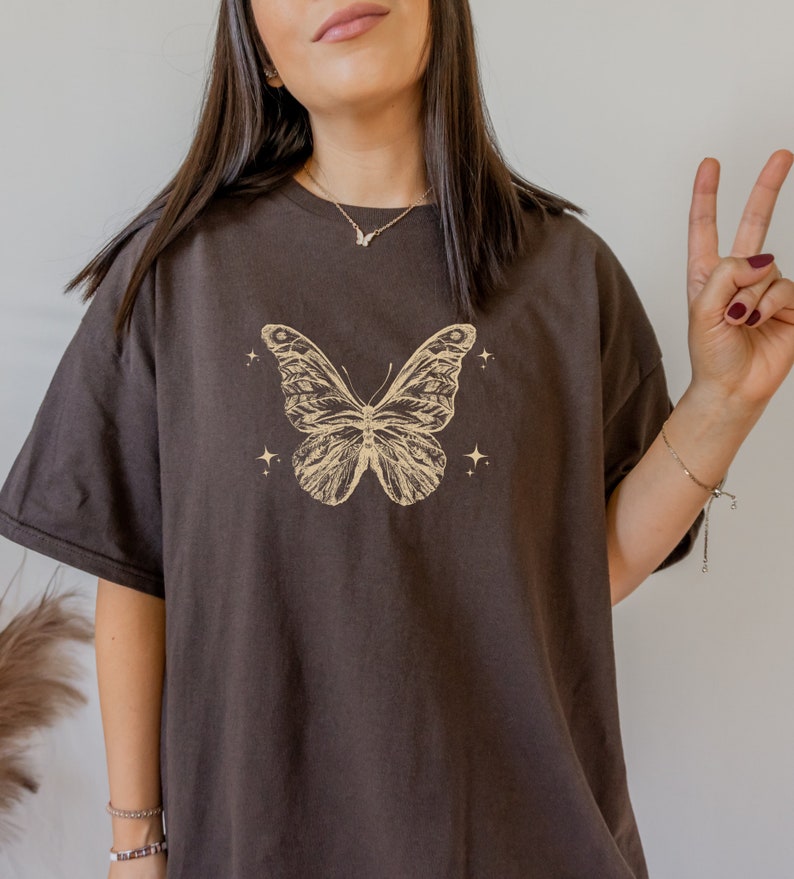 May include: An oversized brown t-shirt with a beige butterfly graphic and small stars on the front.