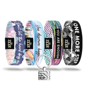 May include: Five colorful fabric bracelets with inspirational quotes, including "Don't let the hard days win" and "You are enough." A silver-colored key chain with a geometric design hangs in front of the bracelets. The bracelets feature various patterns and colors.