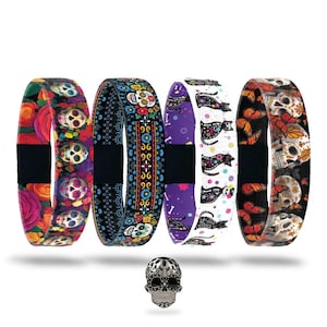 May include: Four colorful elastic bracelets with Day of the Dead themes, featuring skulls, flowers, and butterflies. A silver skull charm is at the bottom. The bracelets have black centers and various patterns in red, purple, and black.