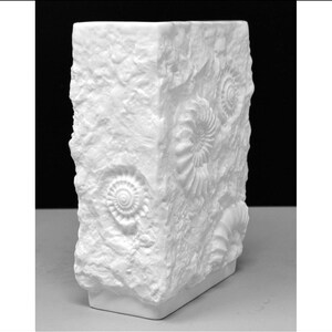 Puede incluir: Jarr&oacute;n rectangular blanco con una superficie texturizada similar a la piedra. El jarr&oacute;n presenta dise&ntilde;os de f&oacute;siles en relieve, agregando una est&eacute;tica natural &uacute;nica. Es un objeto decorativo.