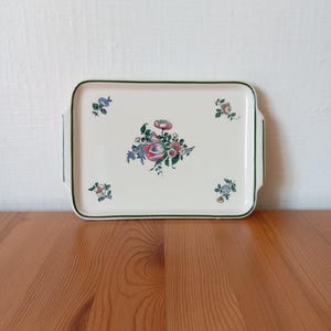 Peut inclure: Plateau de service rectangulaire crème, orné d'un bouquet floral central et de petits groupes floraux aux coins. Le plateau a une bordure et des poignées vertes, posé sur une surface en bois.