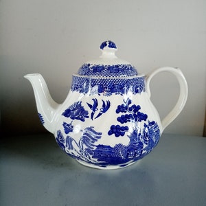 May include: A white teapot with a blue and white willow pattern. The teapot has a lid and a handle.