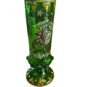 May include: A green glass vase with a painted design of a knight in armour holding a sword and shield. The vase has a flared base with a decorative pattern.
