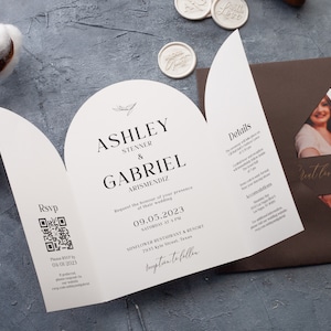 May include: A tri-fold wedding invitation with a brown envelope. The invitation features the names Ashley Stenner & Gabriel Arismendiz, date, time, and location. The invitation includes a QR code for RSVP and details.