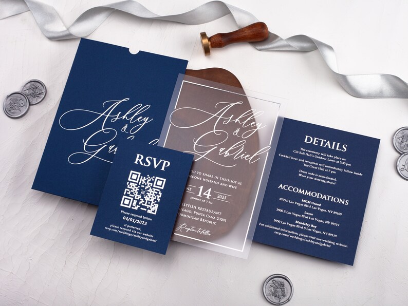 May include: A navy blue wedding invitation suite with a clear acrylic invitation card featuring the names "Ashley & Gabriel" in white cursive script. The RSVP card has a QR code and the text "Please respond by 04/01/2023". The details card has the text "DETAILS" and "ACCOMMODATIONS" in white.