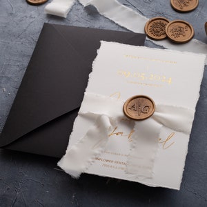May include: Elegant wedding invitation suite featuring a white card with gold foil text, a black envelope, and a white ribbon. The invitation includes the date 09.05.2024 and is sealed with a wax stamp. Additional wax seals are visible.