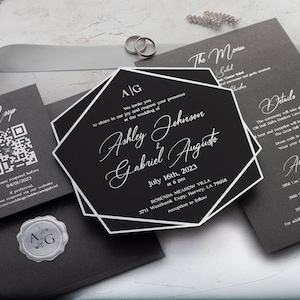 May include: Elegant black and white wedding invitation suite. Includes an invitation with the names Ashley Johnson & Gabriel Augusto, RSVP card with a QR code, menu, details card, and envelope with a wax seal. Silver rings and decorative beads are also present.