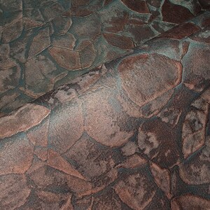 May include: Close-up of a textured fabric with a pattern of overlapping, irregular shapes in shades of brown and teal.