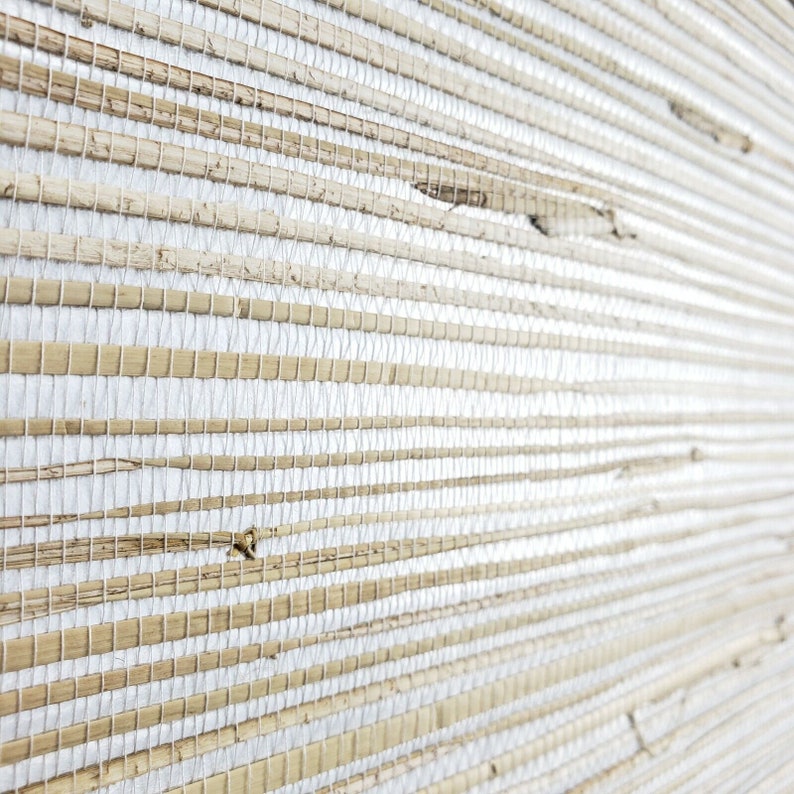 Może przedstawiać: Zbliżenie na tkaną okładzinę ścienną w naturalnym, jasnobrązowym kolorze na białym tle. Splot wykonany jest z cienkich pask&oacute;w naturalnego materiału, tworząc teksturalną powierzchnię.