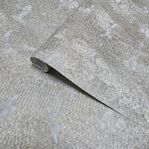 May include: A roll of textured wallpaper in shades of gray and silver. The pattern resembles a scaled or textured design, with a subtle sheen. The paper is partially unrolled, revealing the pattern and texture.