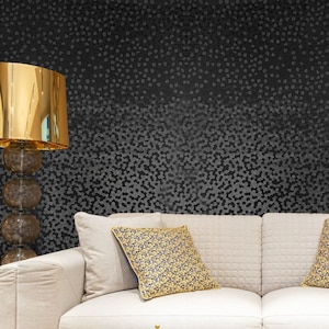 May include: A white couch with two pillows, one with a gold and blue pattern. The couch is in front of a black wall with a white geometric pattern.