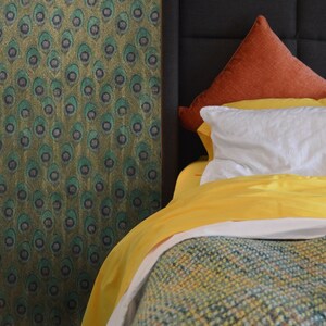 May include: A yellow and white bedspread with a green and brown patterned headboard. The bed is made with a white duvet cover and a rust-colored throw pillow.