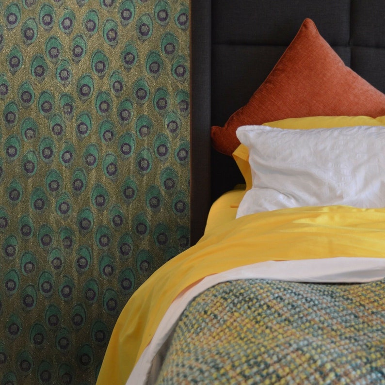 May include: A yellow and white bedspread with a green and brown patterned headboard. The bed is made with a white duvet cover and a rust-colored throw pillow.